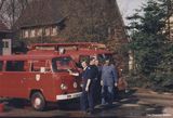 Vier Feuerwehrmänner vor zwei Feuerwehrfahrzeugen